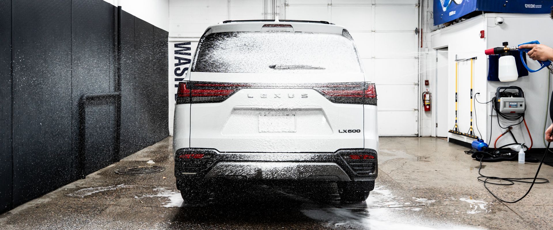 A white SUV covered in foam being washed in a carwash bay.