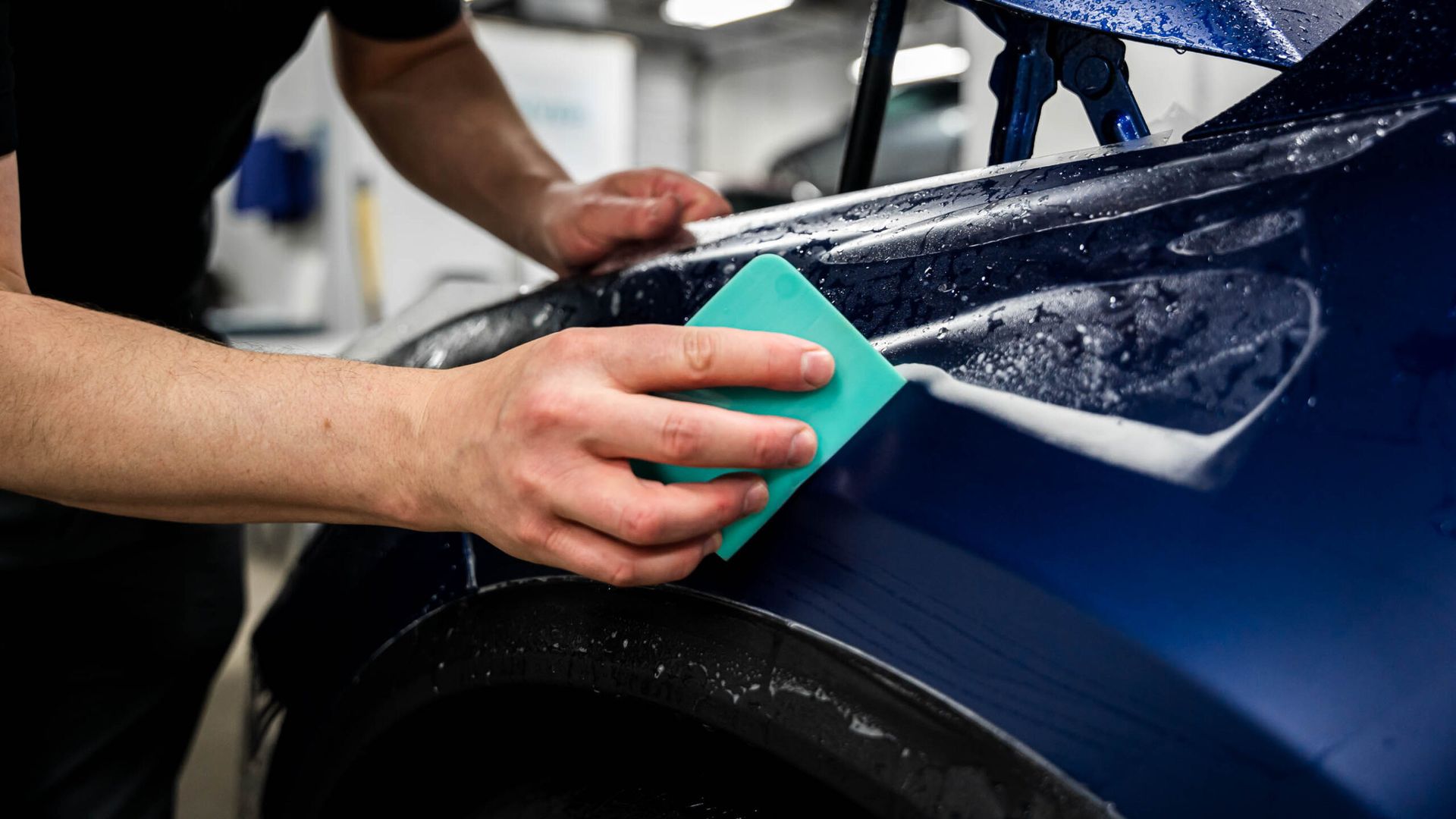 A man is cleaning a blue car with a green sponge.