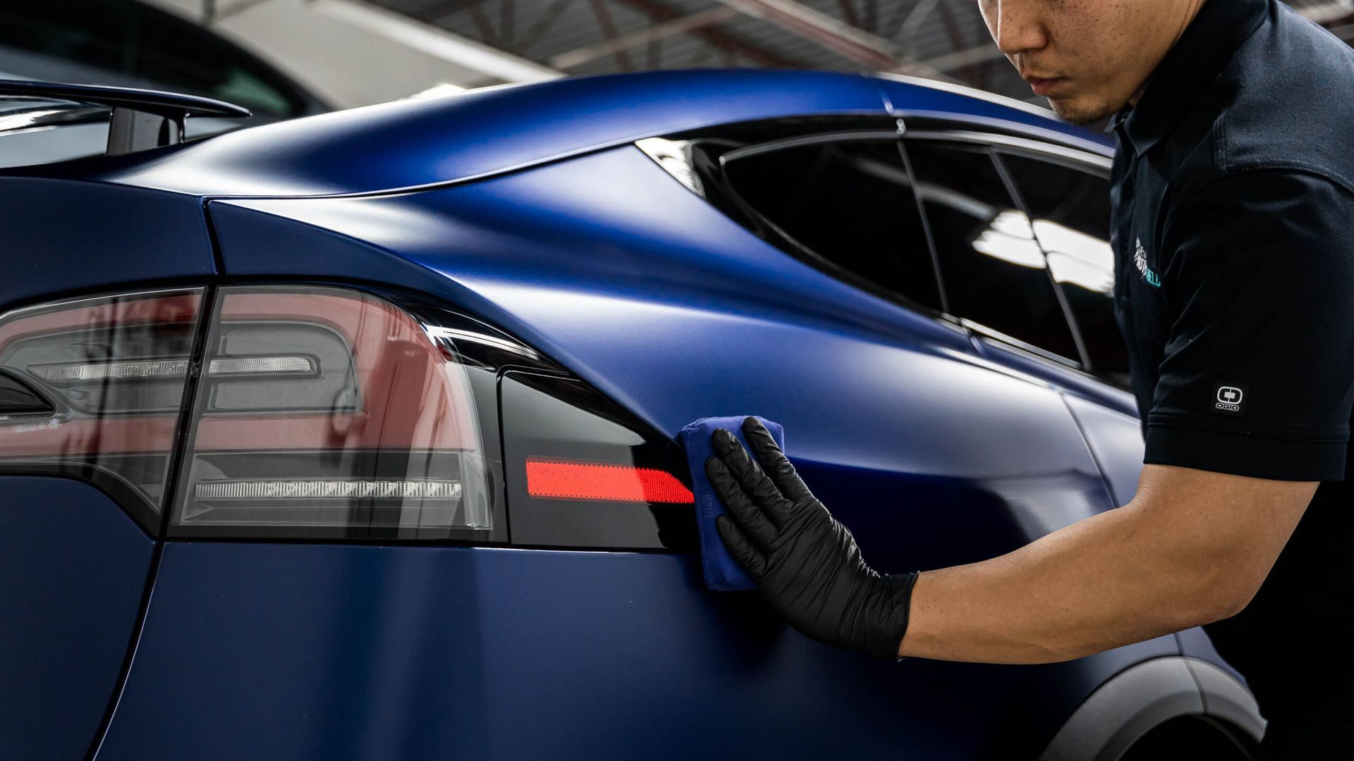 A man is cleaning the side of a blue car with a cloth.