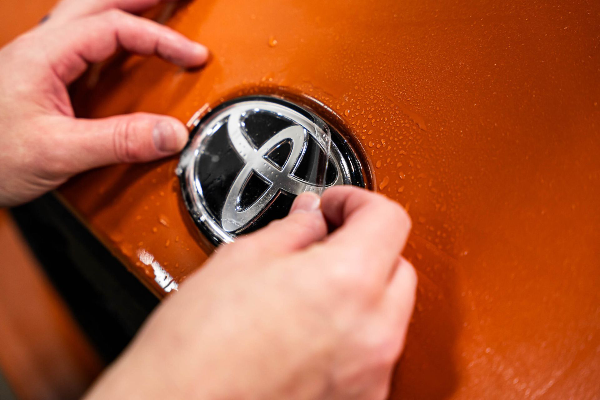 A person is putting a toyota logo on a car.