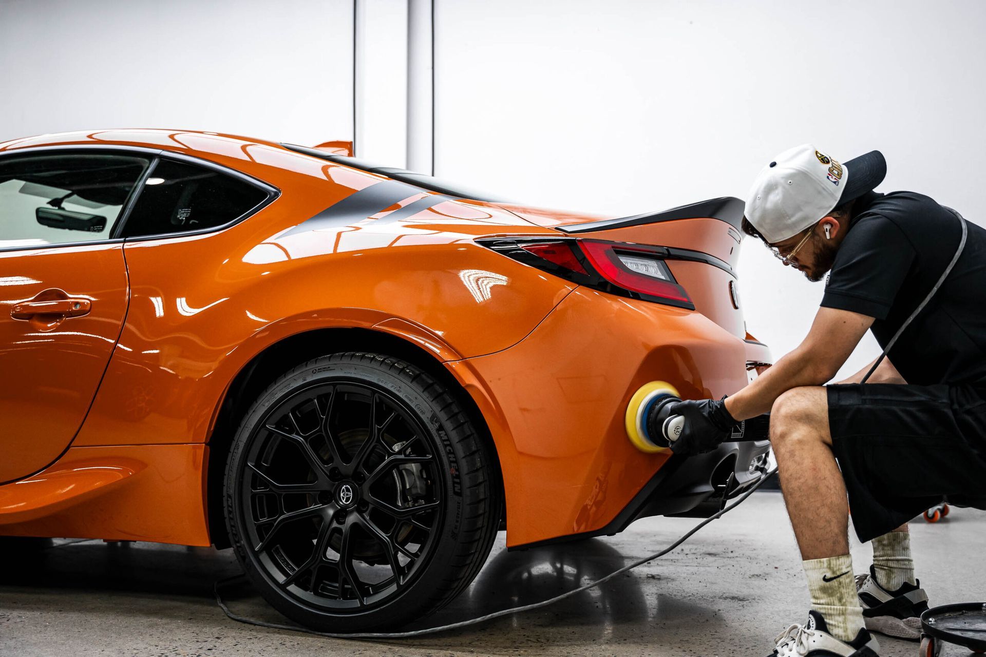 A man is polishing the back of an orange sports car.