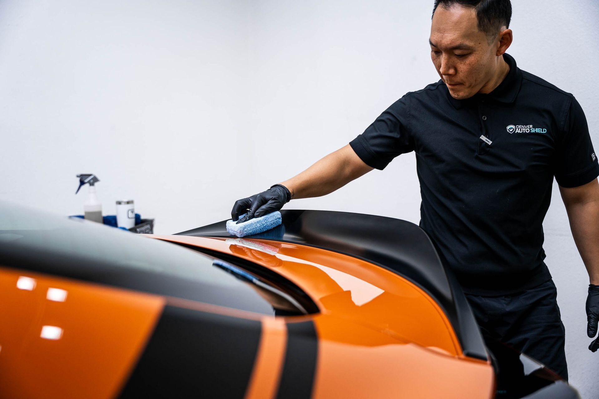A man is cleaning the hood of an orange car.