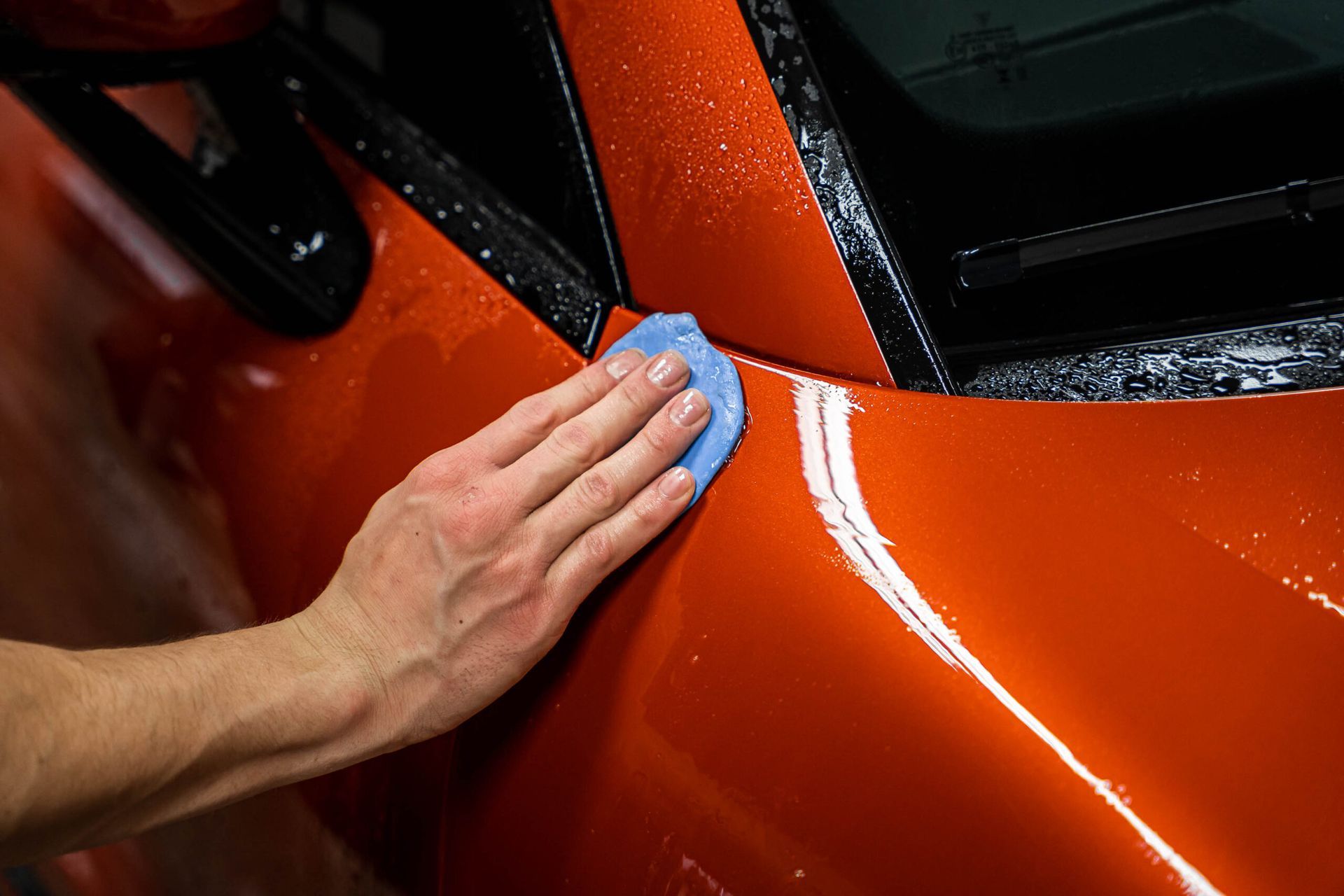 A person is applying wax to the side of a red car.