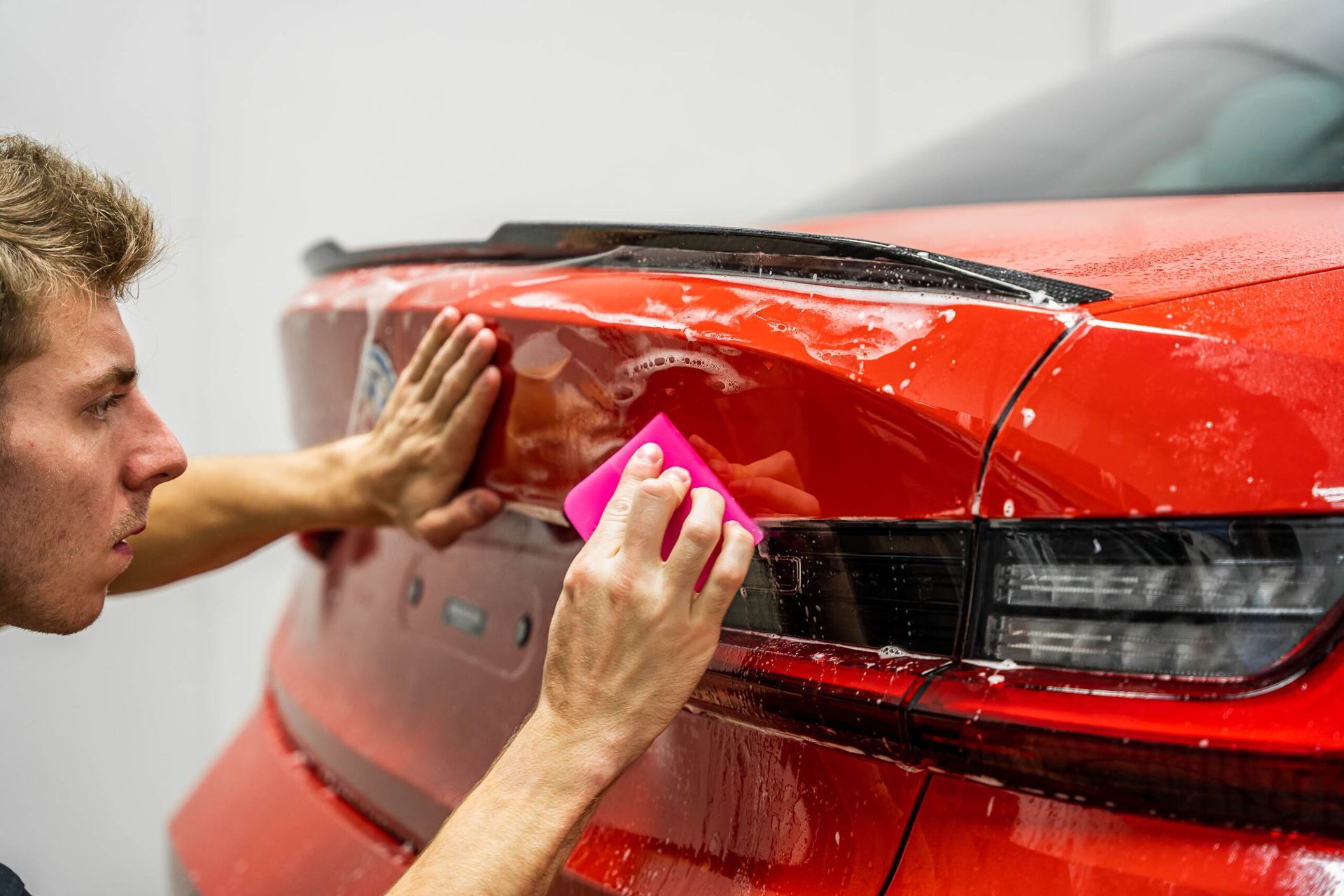 A man is applying a protective film to the back of a red car.