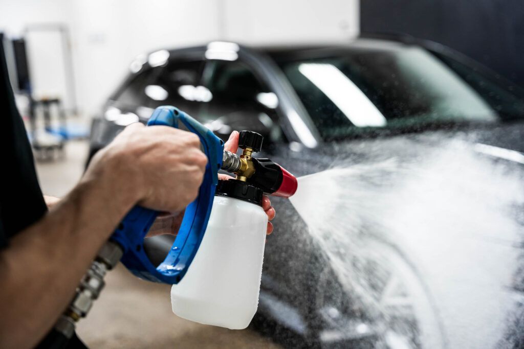 A person is spraying water on a car with a spray bottle.