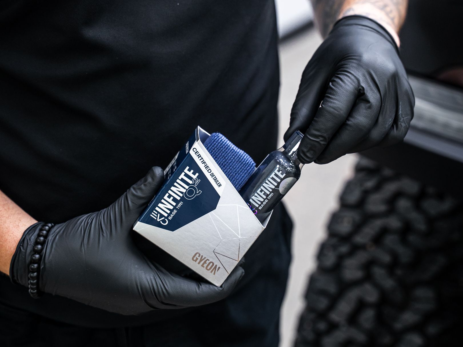 A person wearing black gloves is holding a box of ceramic coating.