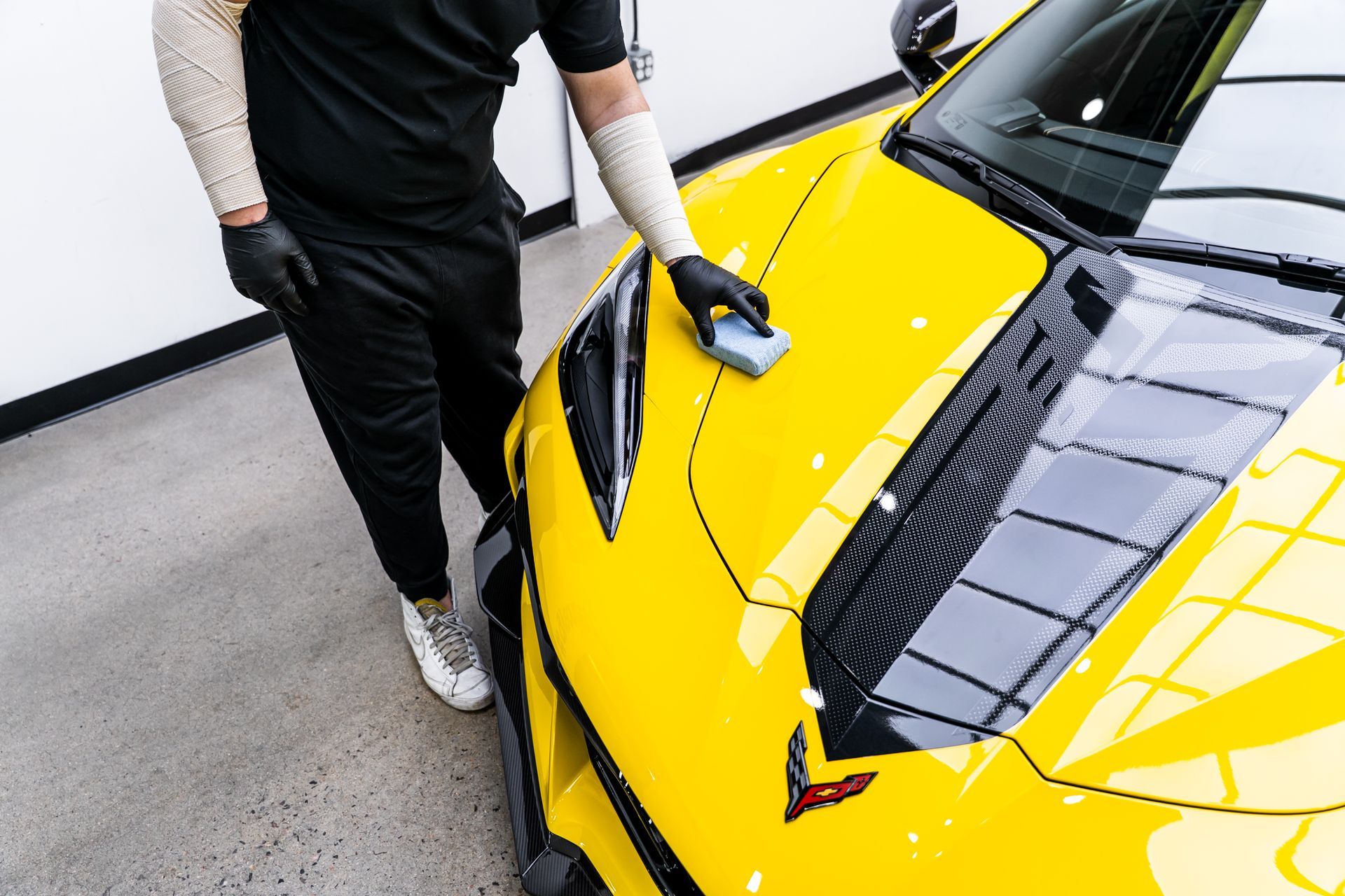 Person applying ceramic coating to yellow sports car, black gloves, sleeves, and sweatpants.