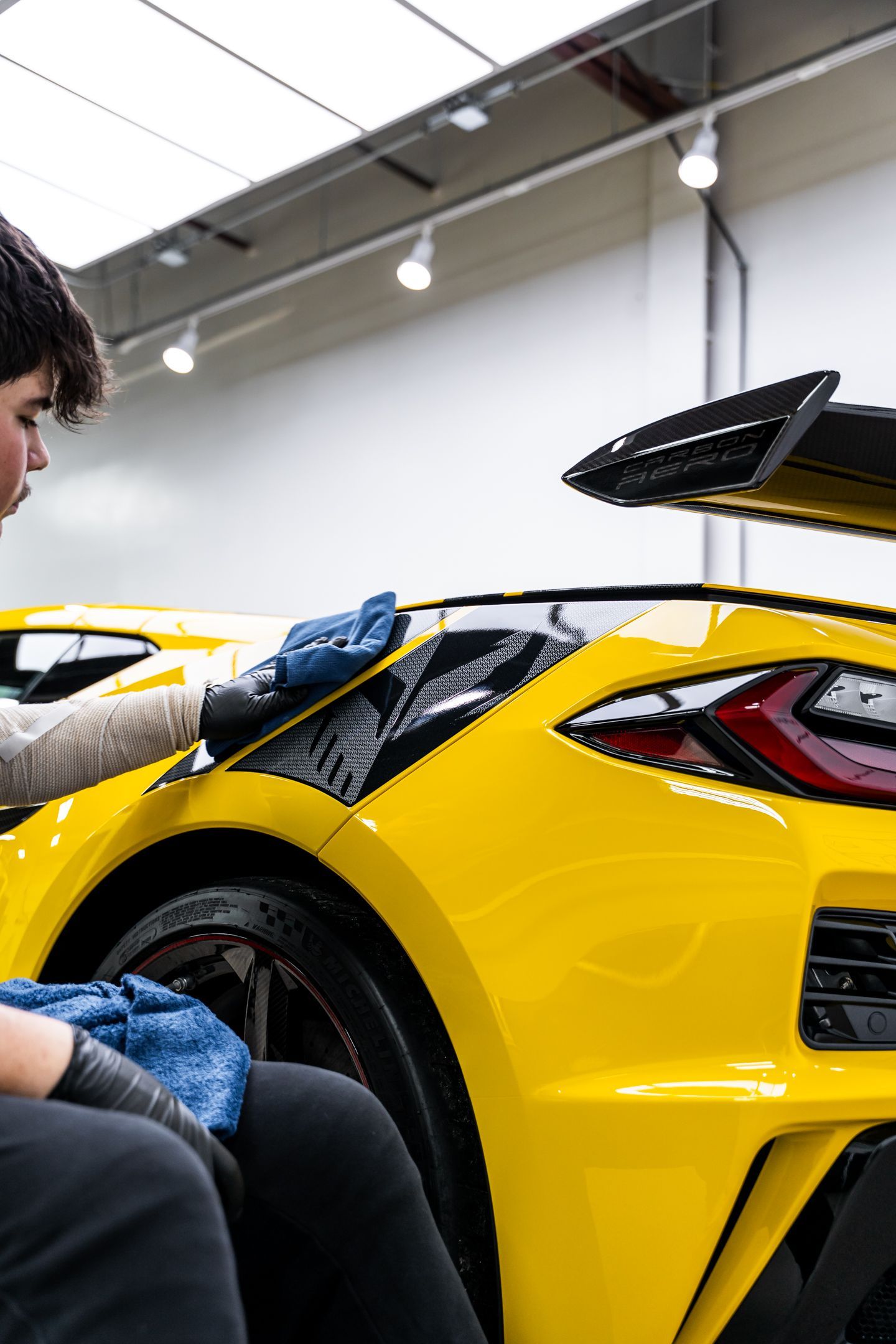 A person in gloves polishing a bright yellow sports car in a well-lit garage.