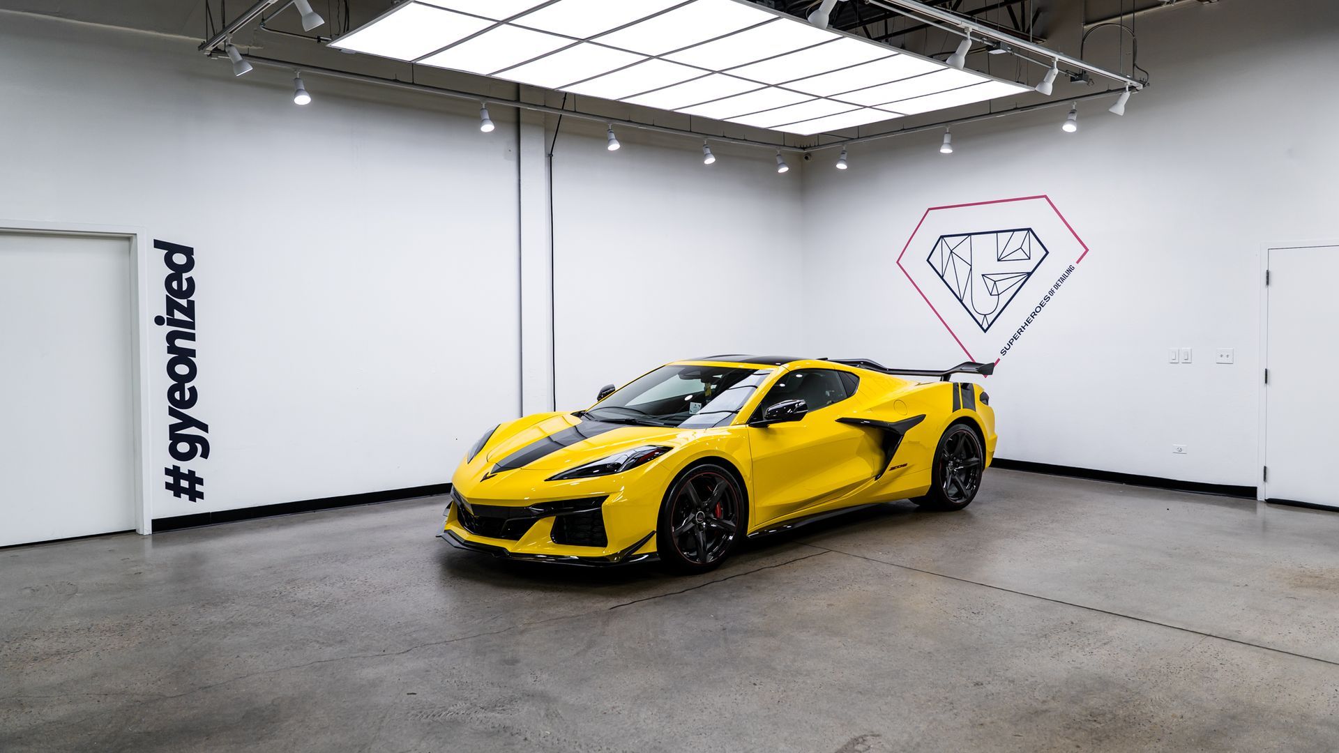 Yellow sports car in a white showroom, black stripe, diamond logo, hashtag, and bright lights.