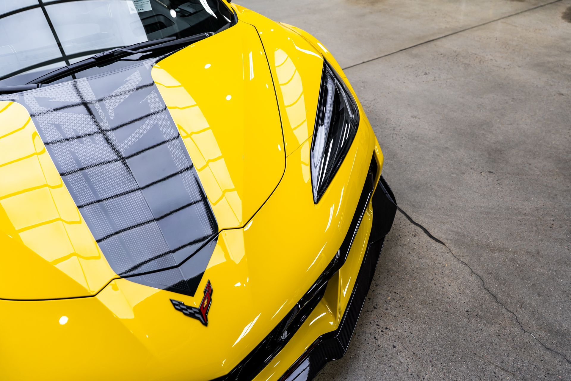 Yellow sports car with black stripe on the hood, parked indoors.