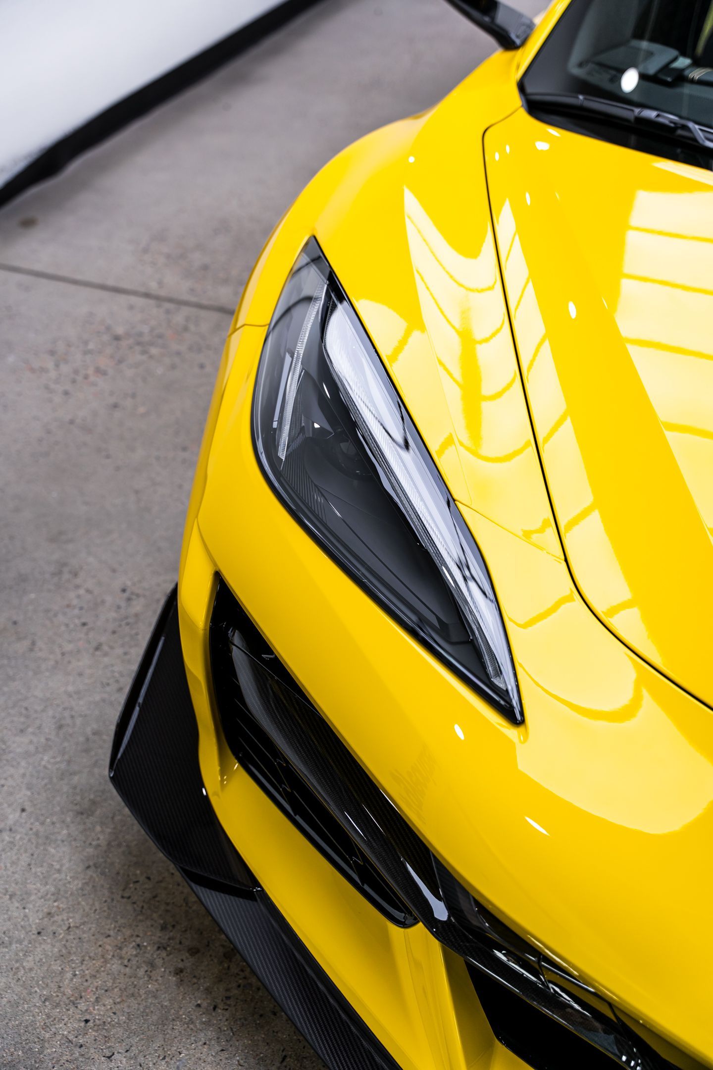 Yellow sports car with black trim, close-up of headlight and front bumper.