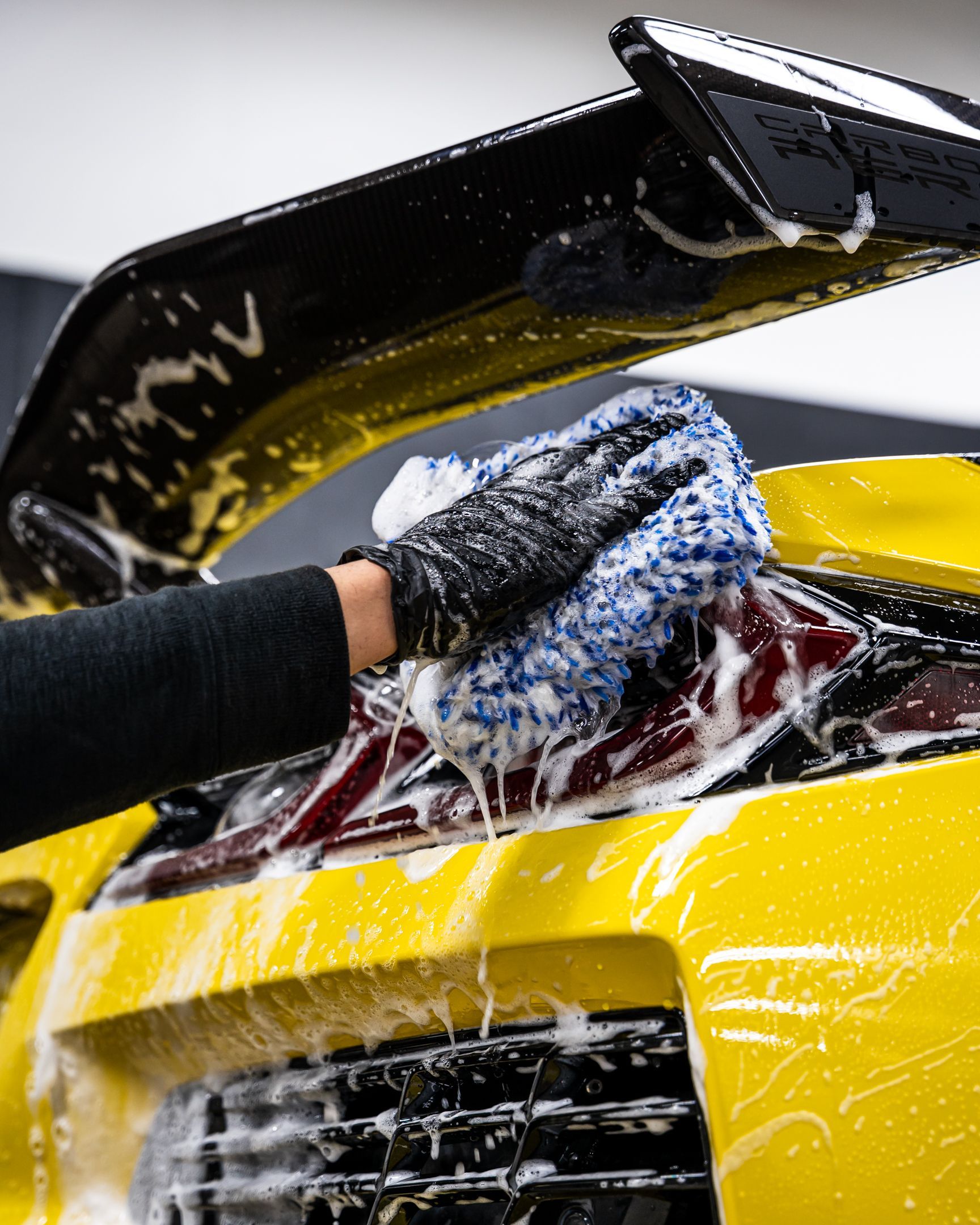 Person washing a yellow sports car with a soapy mitt.