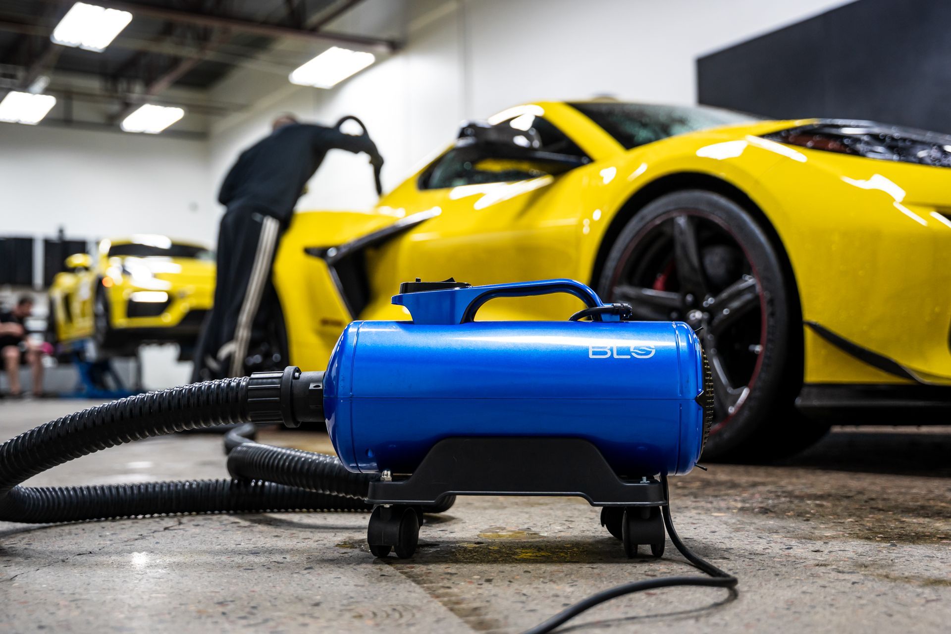 Blue car dryer being used on a bright yellow sports car in a garage.