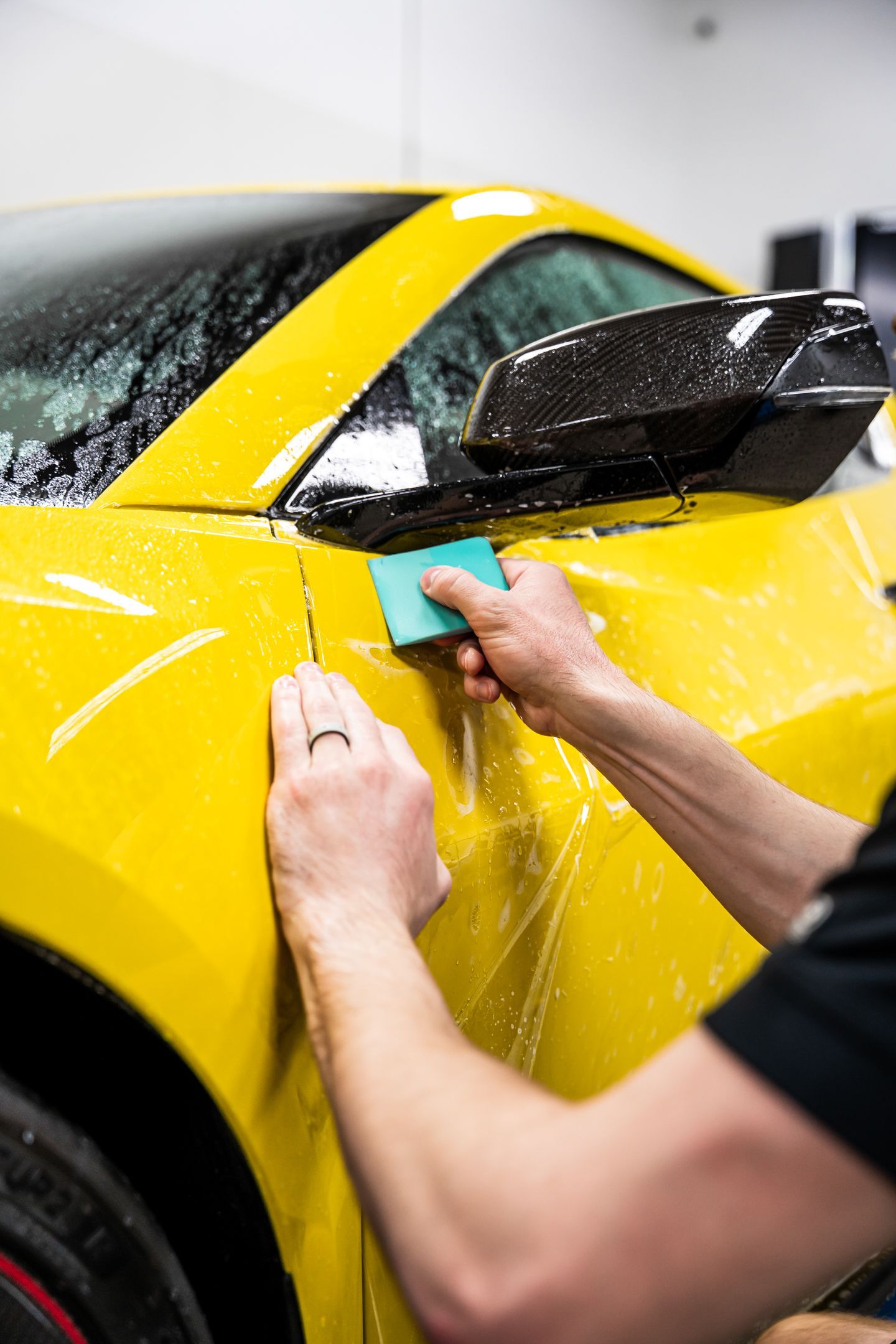 Person applying film to a yellow car, using a squeegee. The setting is indoors.