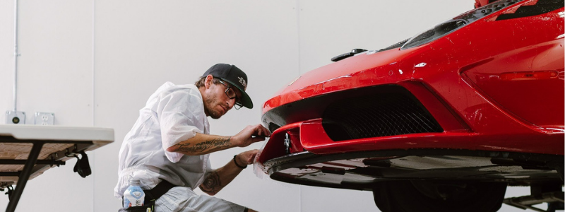 A man is working on the front of a red sports car.