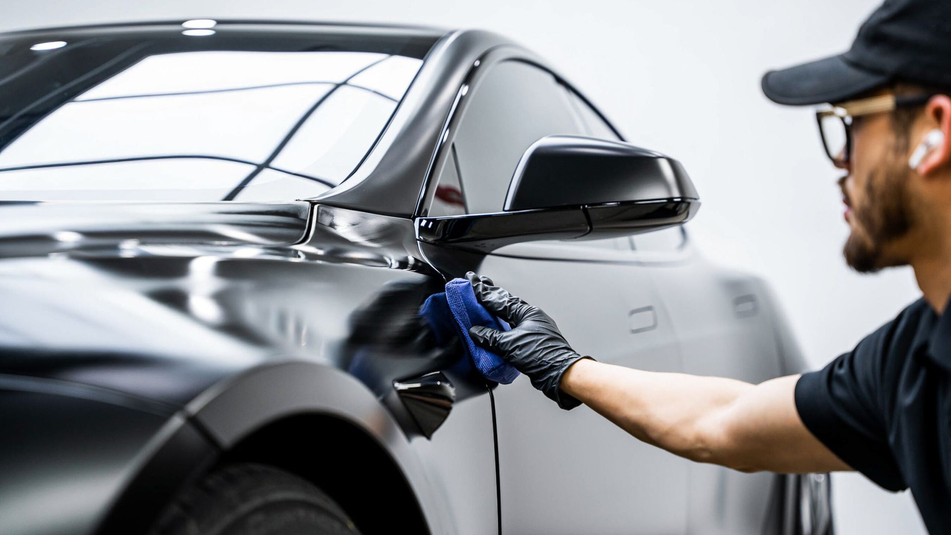 A man is cleaning the side of a car with a cloth.