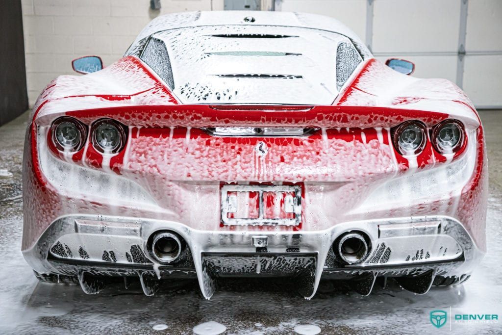 A red sports car is covered in foam in a garage.