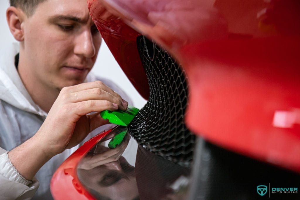 A man is working on the front of a red car.