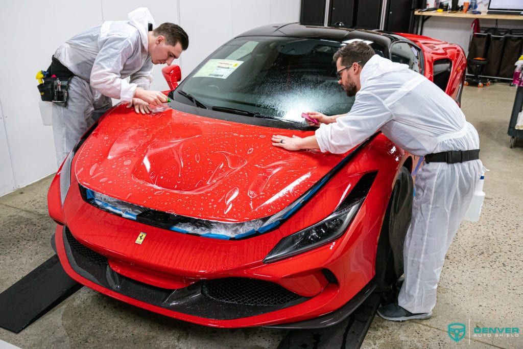 Two men are working on a red sports car in a garage.