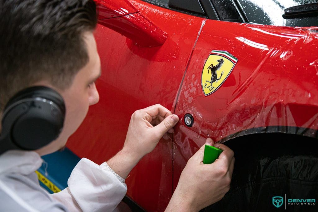A man wearing headphones is working on a red ferrari car.