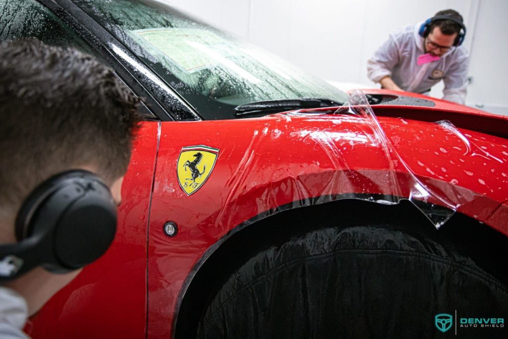 A man wearing headphones is looking at a red ferrari car.