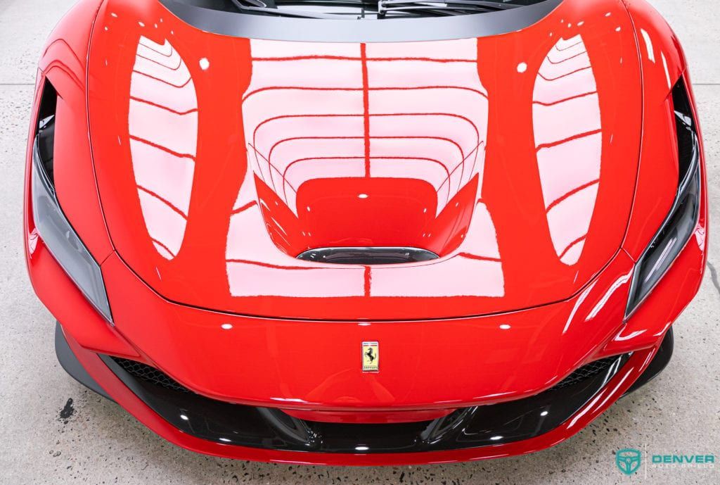 The front of a red ferrari sports car with a white stripe on the hood.