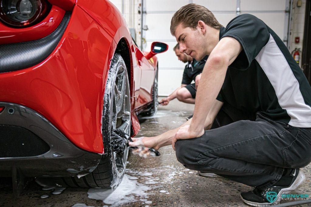 Two men are washing a red sports car in a garage.