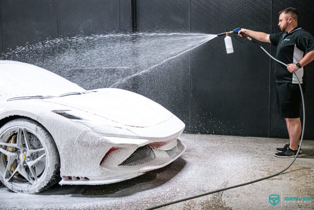 A man is spraying foam on a white sports car.