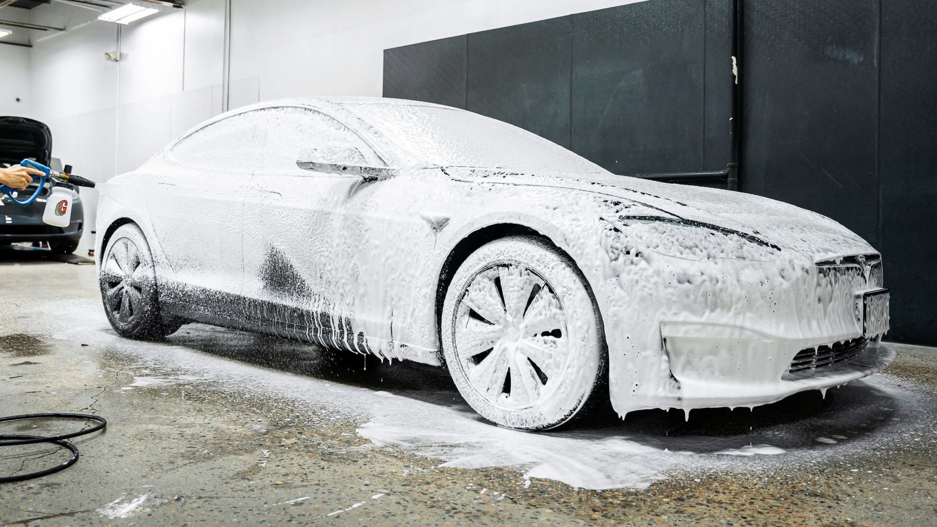 A tesla model s is covered in foam in a garage.