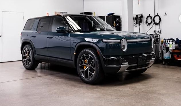 Dark blue SUV parked indoors in a garage, front-left view, with wall-mounted tools in the background