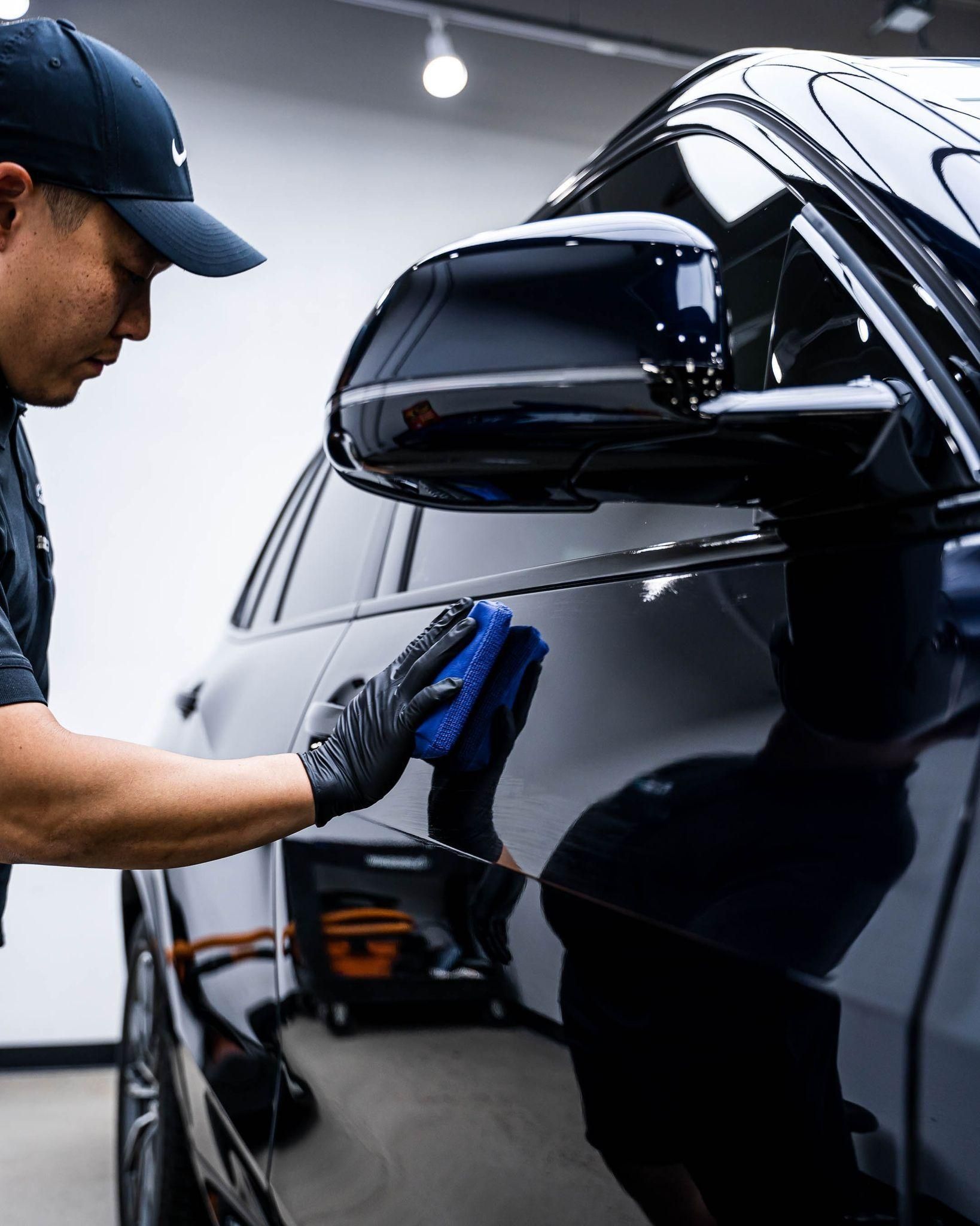 Detailing worker polishing a black car’s side panel in a garage