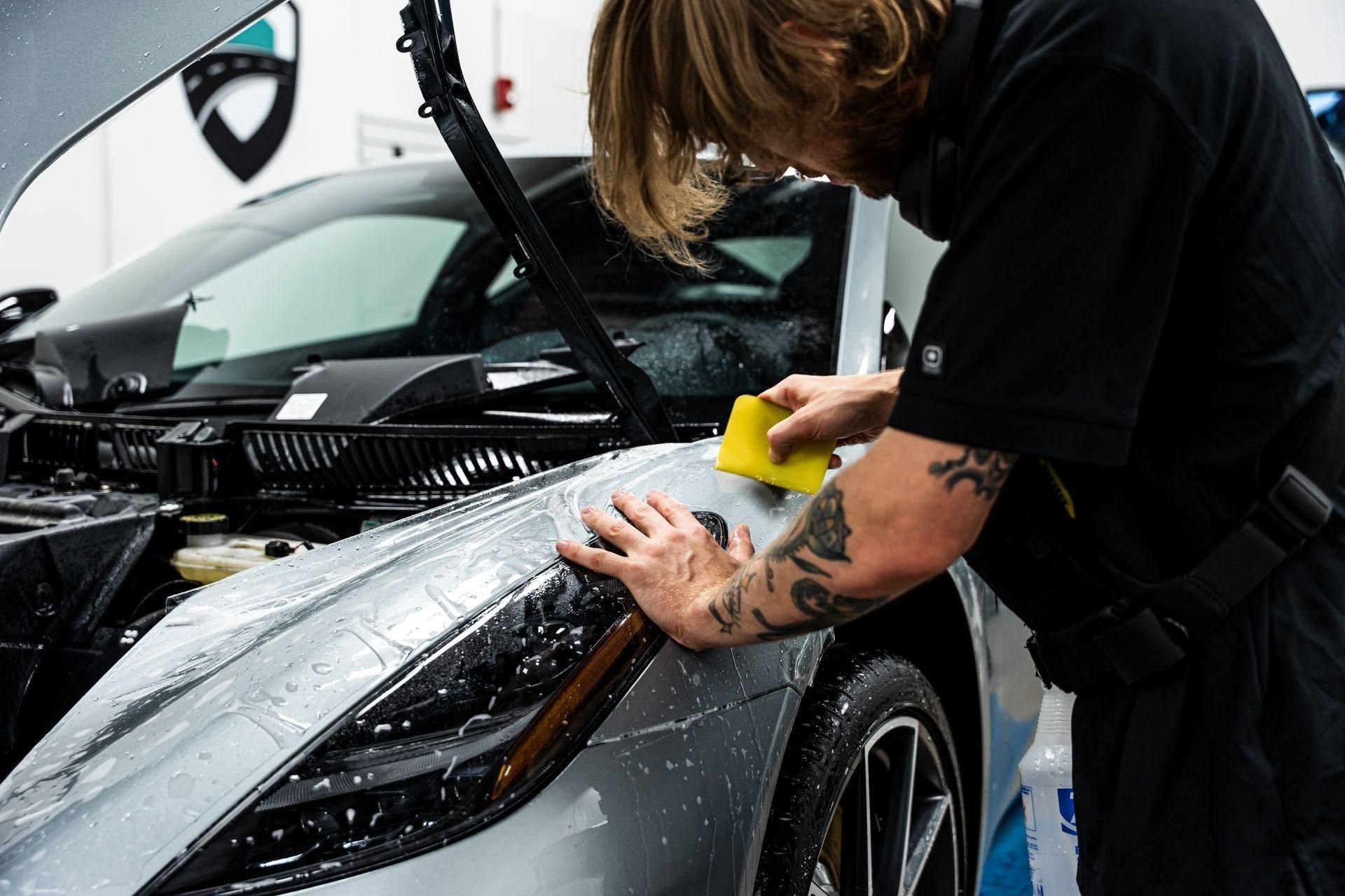 Detailing a silver car’s hood with a cloth in a workshop