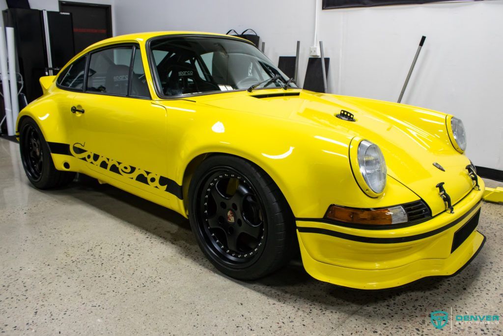 A yellow porsche 911 is parked in a garage.