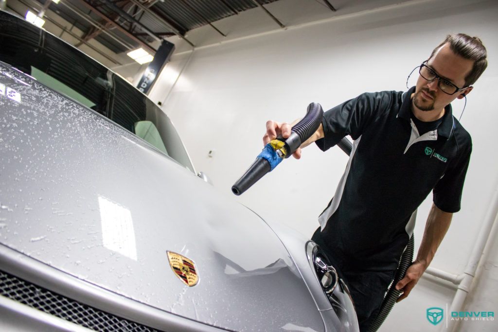 A man is cleaning the hood of a car with a blower.