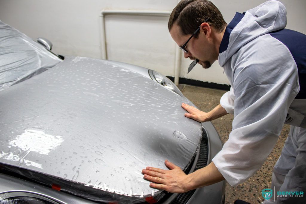 A man is applying a protective film to the hood of a car.