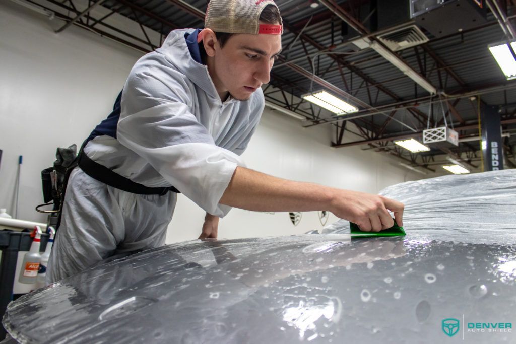 A man is wrapping a car in plastic in a garage.
