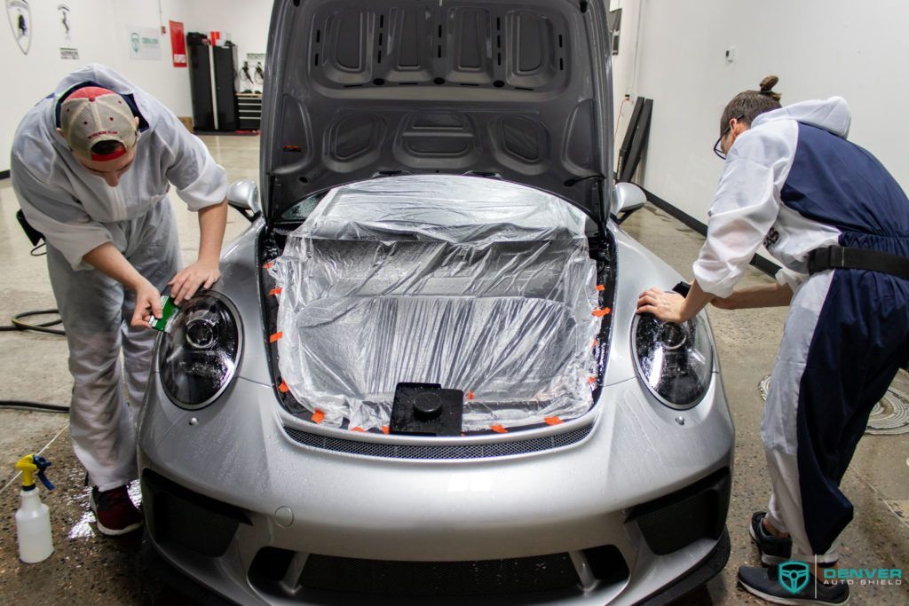Two men are working on a silver car in a garage.