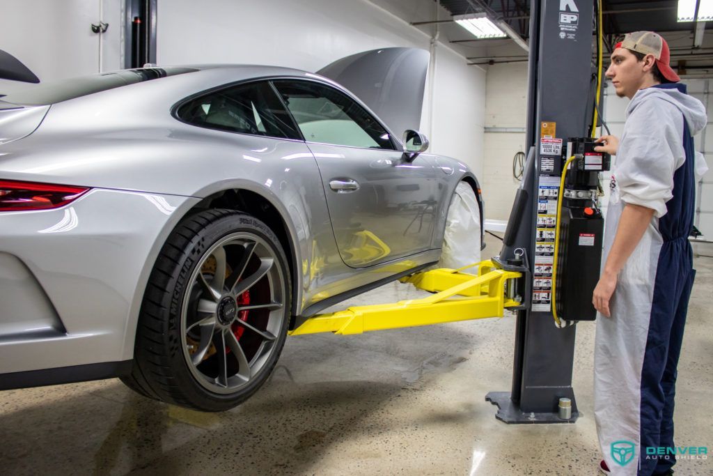 A man is standing next to a car on a lift in a garage.