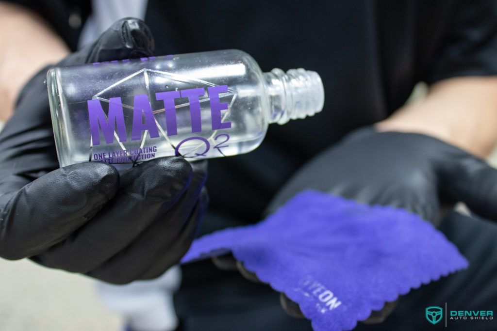 A person wearing black gloves is holding a bottle of matte on a purple cloth.
