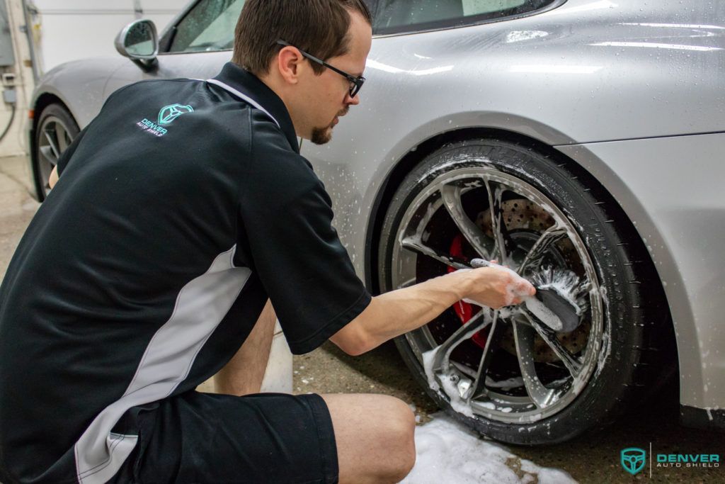 A man is cleaning a car wheel with a brush.