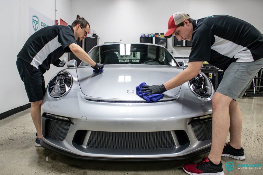 Two men are cleaning a silver sports car in a garage.