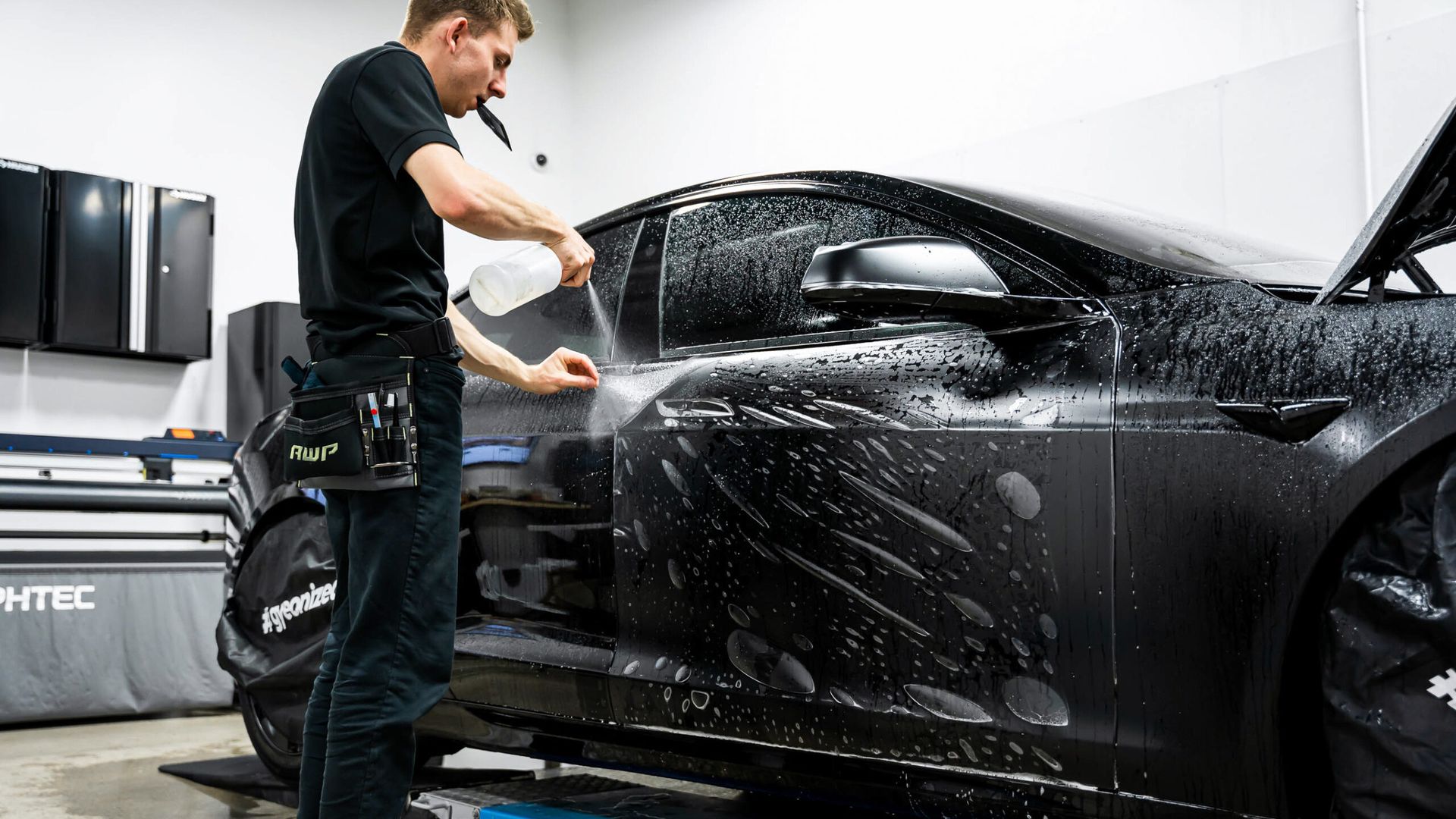 A man is wrapping a black car with a protective film.