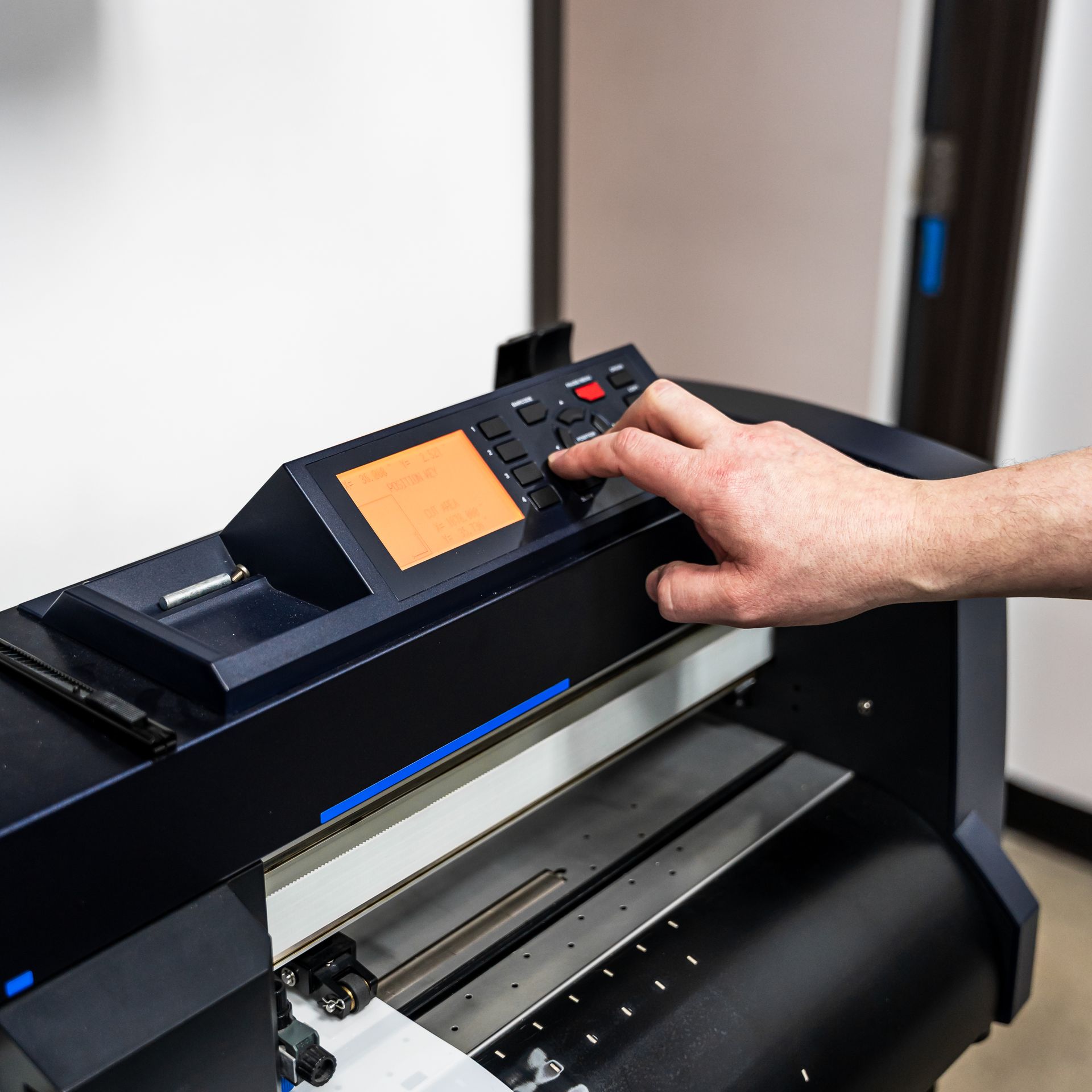 A person operates a black vinyl cutter. Their hand presses buttons on the control panel.