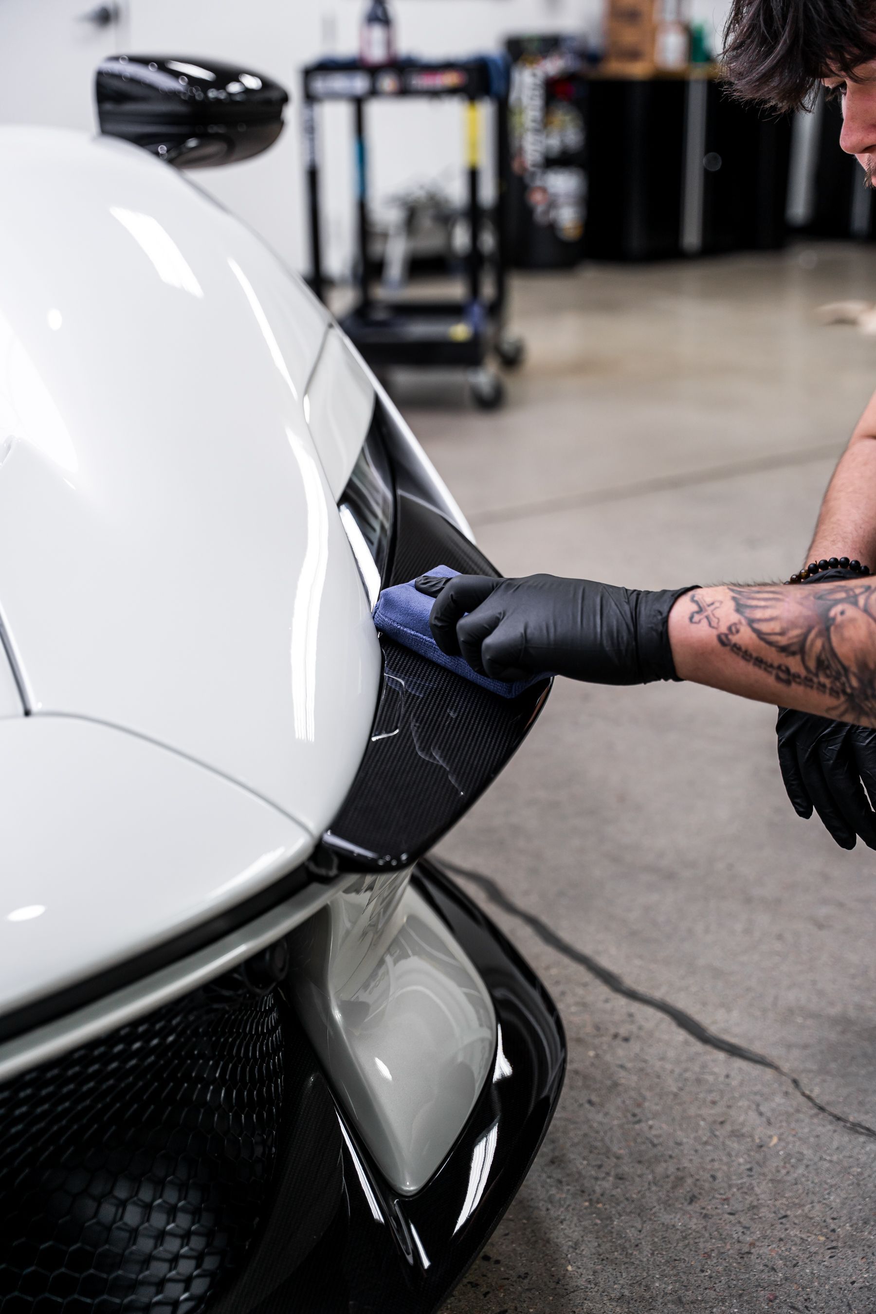 Person in black gloves polishing a white car with black accents.
