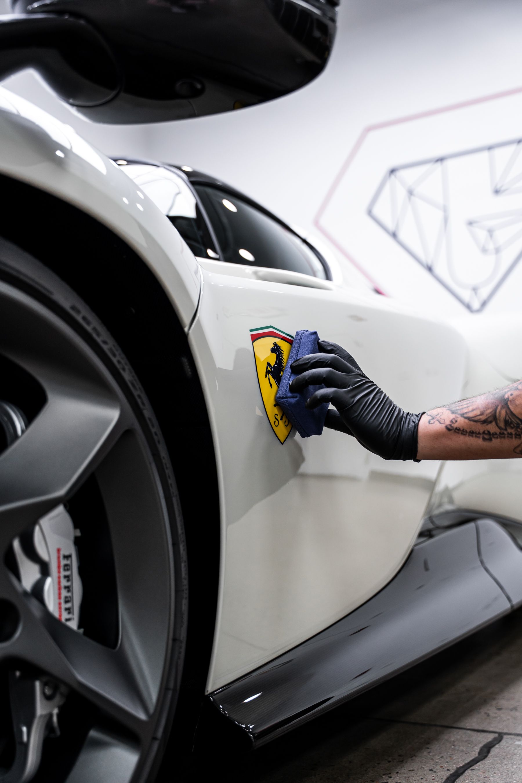 A person in black gloves applying detail to a white Ferrari with the emblem.