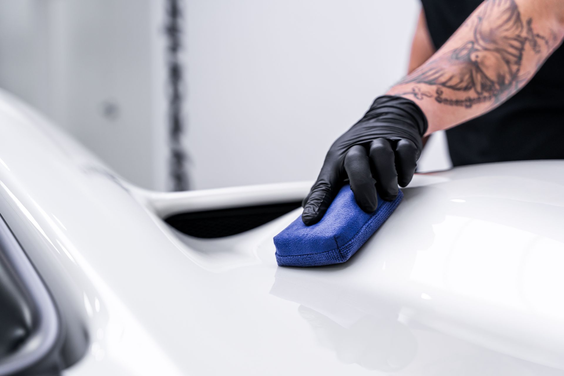 Person applying ceramic coating to white car with a blue applicator pad.