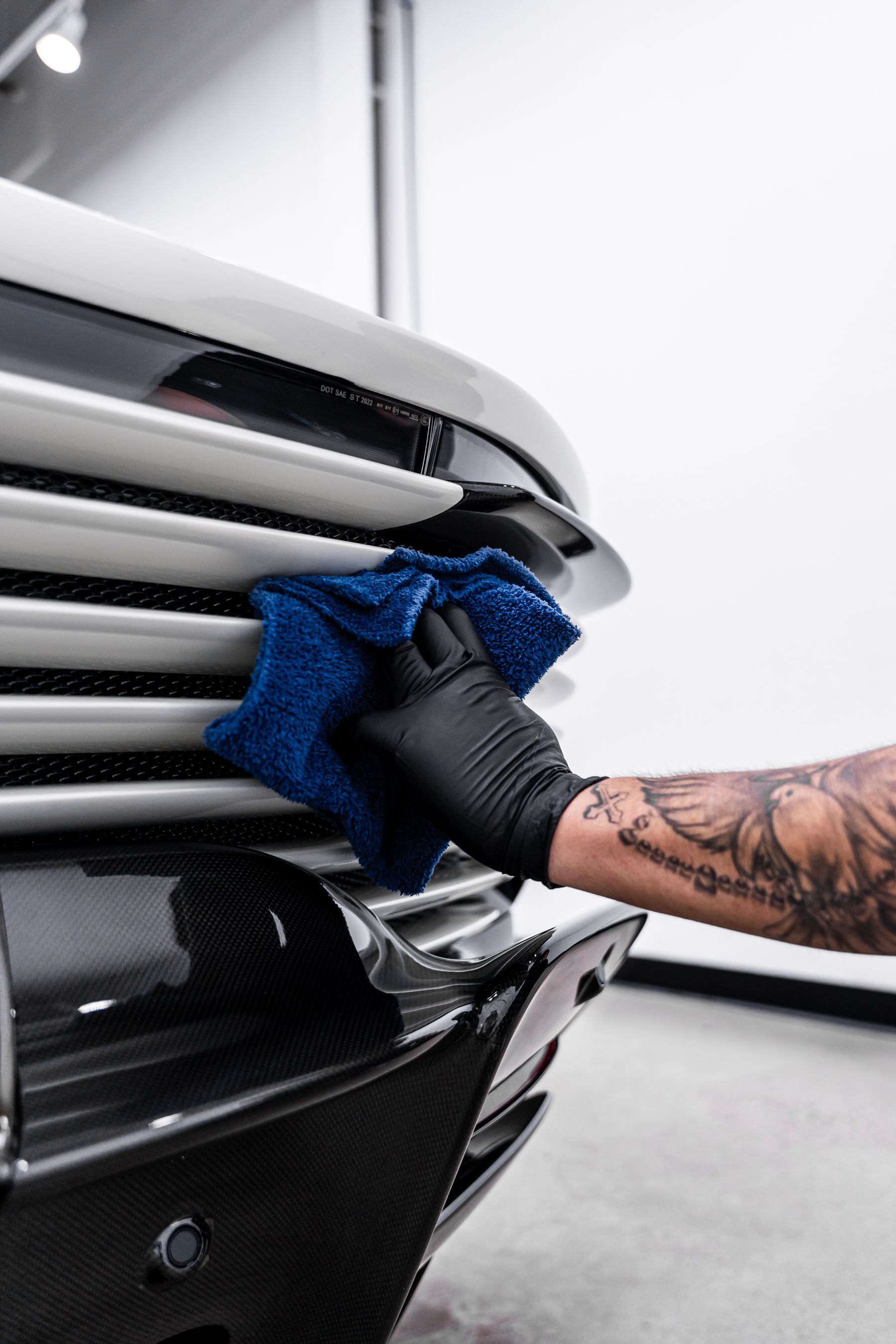 Person in black glove wiping car's silver grill with a blue microfiber cloth.