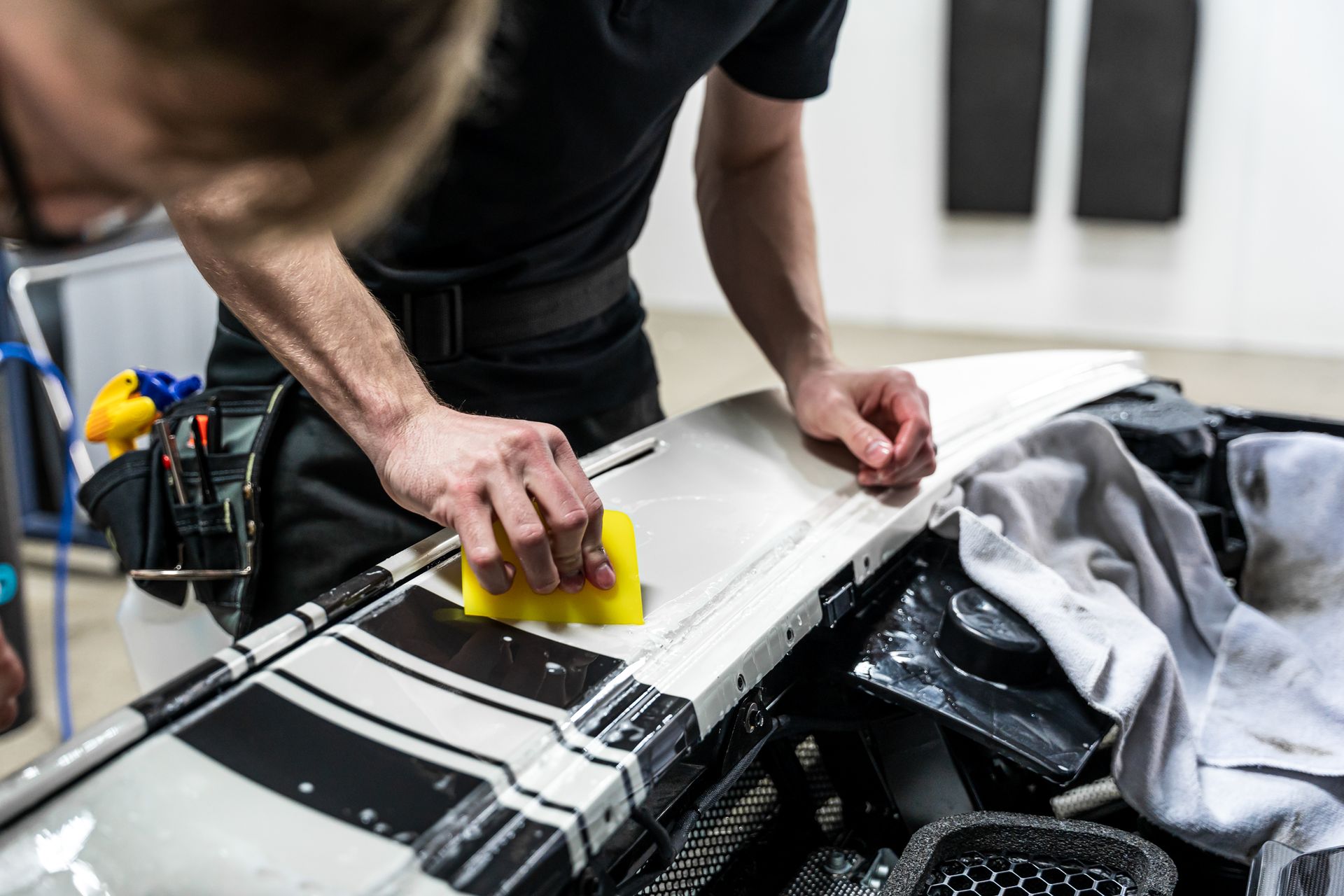 Person applying wrap on a car part with yellow applicator. Workshop setting.