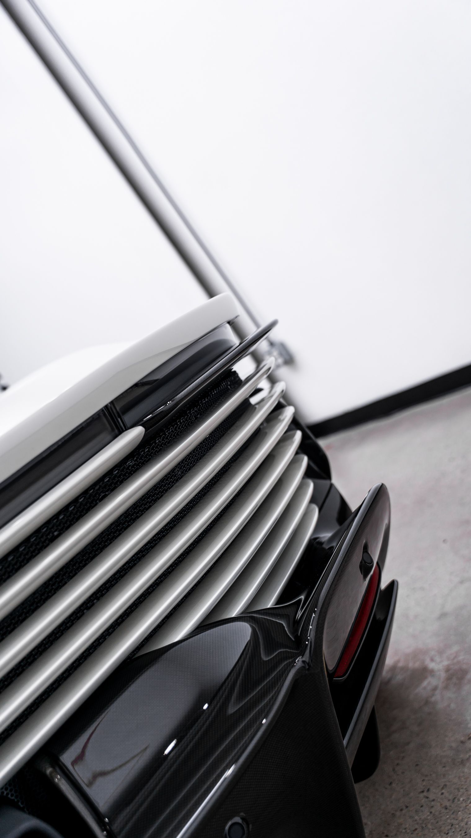 Close-up of a car's front grill with horizontal slats, angled against a bright, blurred background.