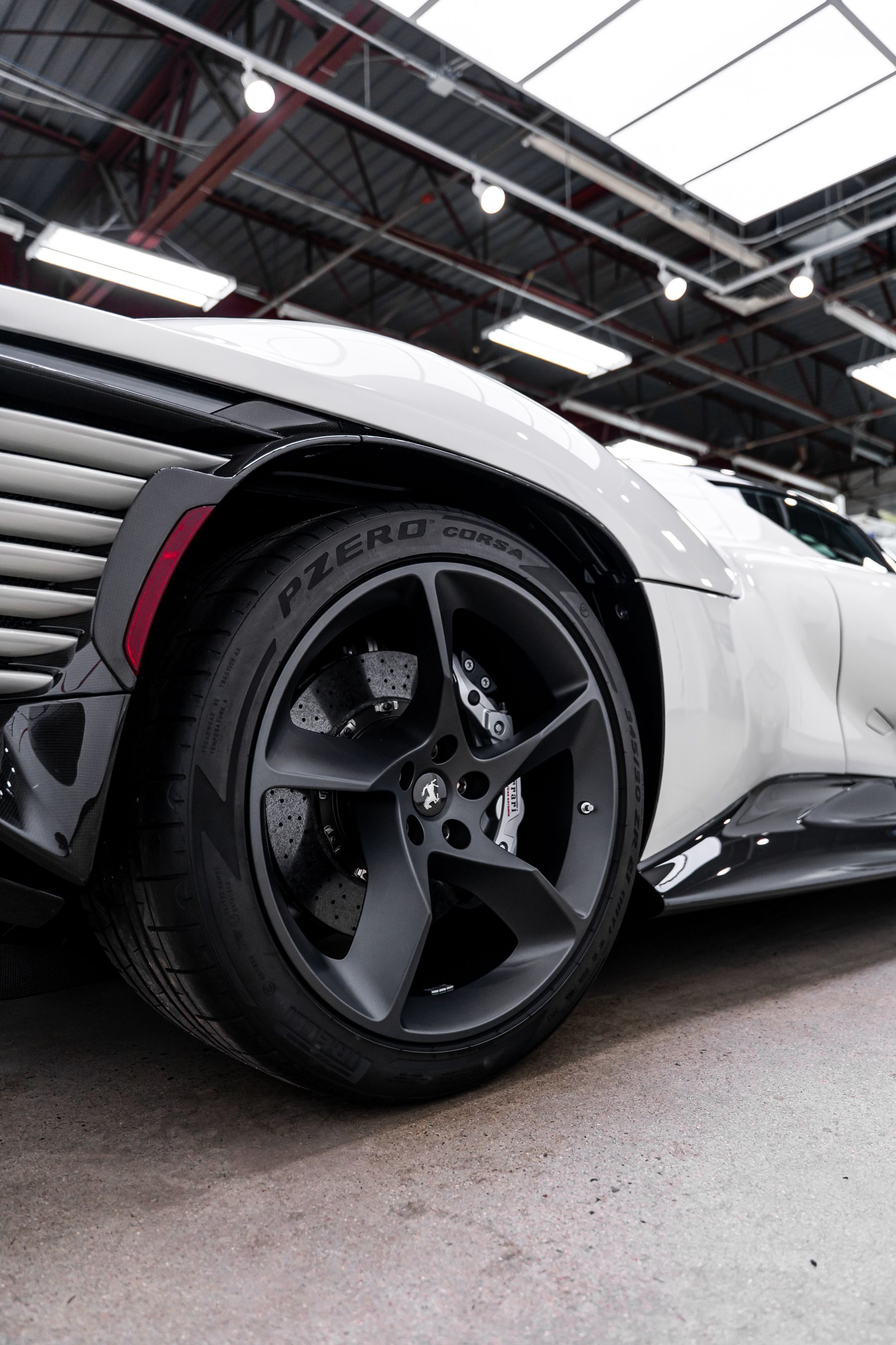 White sports car's front wheel and body with black rims and accents, indoors.